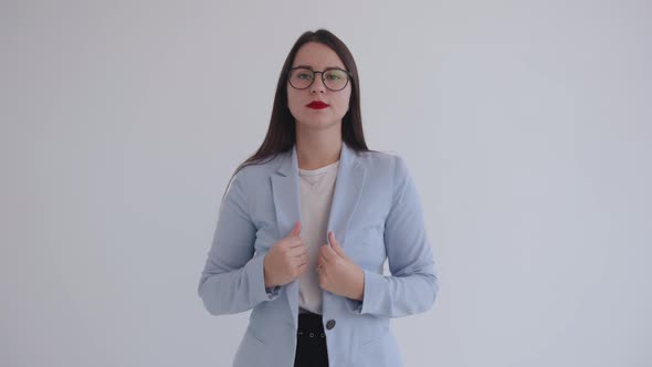 A Confident Young Business Lady in Black Glasses Stands on a White Background and Straightens Her