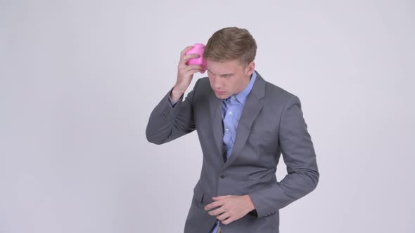 Young Stressed Businessman Holding Piggy Bank and Giving Thumbs Down