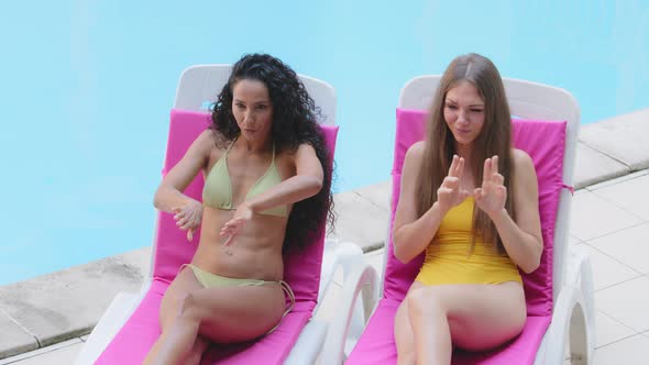 Cheerful Millennial Tanned Young Girls in Swimsuits Sitting in Sun Loungers Have Fun Dancing