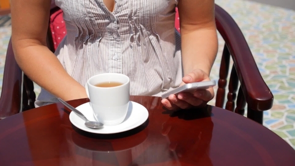 Young Woman Using Phone And Drinking Tea In Cafe