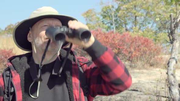 An older hiker looking through binoculars while on a scenic hike in the mountains.