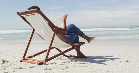 African american woman reading and lying on sunbed on sunny beach