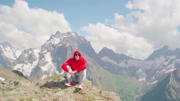 Young Man in Sunglasses Sitting on Mountain in Sunny Weather