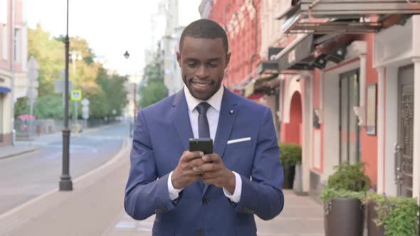 African Businessman Using Smartphone While Walking to Office