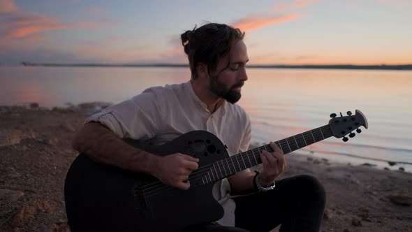 Silhouette of a Young Man Sitting on the Beach By the Water Playing Guitar