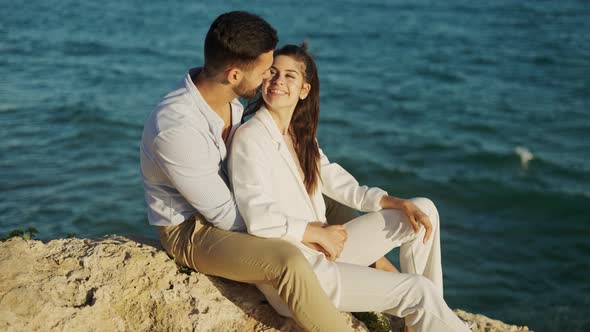 Smiling Ethnic Couple Talking on Rock Against Sea