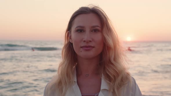 Young Blonde Woman with Wavy Hair Standing on Beach By the Sea on Sunset