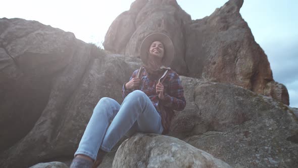 Girl Hiker with Backpack Sits on Edge of Cliff and Looks Into Distance Mountain View Travel and