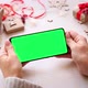 Woman holding smartphone with horizontal green screen on Christmas background with gifts. - VideoHive Item for Sale