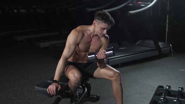 Athletic Man Trains in the Gym Lifts Dumbbells and Performs Hand Exercises Cinematic Light Slow