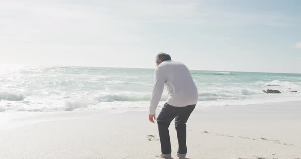 Back view of hispanic senior man sitting on beach at sunset