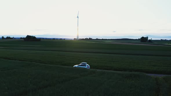 A Car with Roof Rack Drives Along a Road Through Green Meadows and Arable Fields