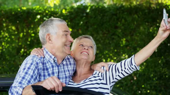 Senior couple taking a selfie on mobile phone near car