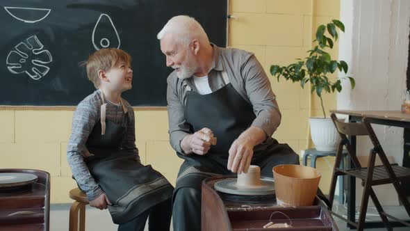 Caring Senior Grandfather Showing Grandson How To Work with Clay on Throwing-wheel in Workshop