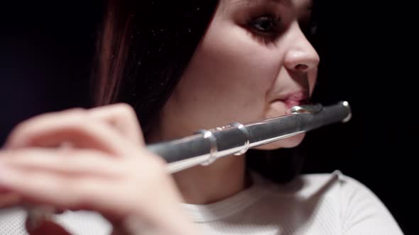 Closeup face of female musician playing flute in studio with dark background. Female musician plays