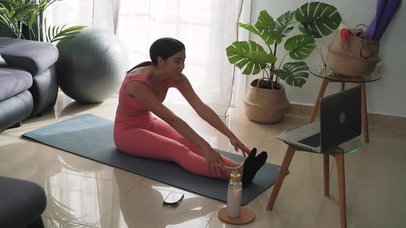 Young Latin woman doing pilates virtual fitness class with laptop at home