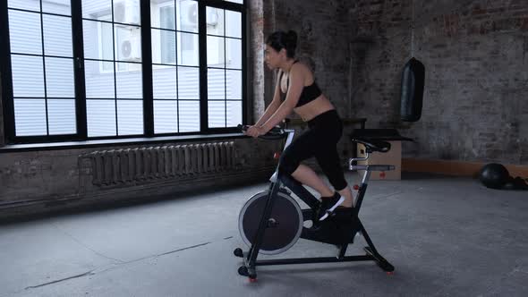 Attractive asian woman biking in the gym, exercising legs doing cardio workout cycling bikes