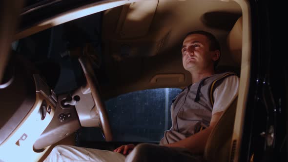 Close Up of Young Man Sitting in Car Behind Wheel and Looking Away in Nighttime
