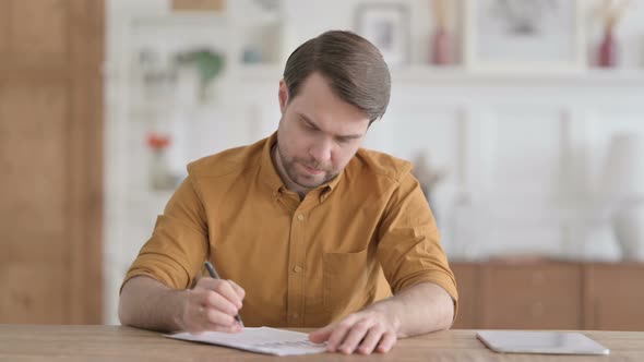 Young Man Writing on Paper in Office
