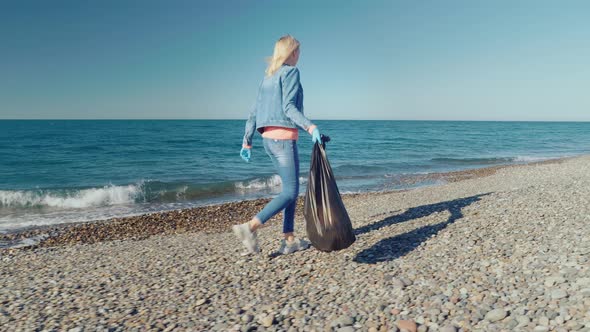 a female volunteer collects garbage in a black garbage bag.