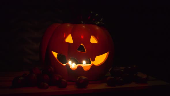 Halloween Pumpkin od dark background with chestnuts, illuminated by candles, dark red glow on black,