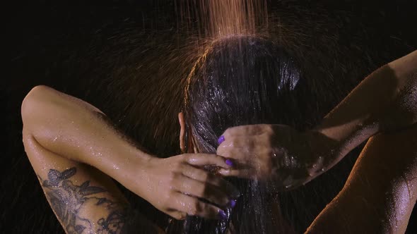 Rear View of a Brunette with Long Hair Who Washes Her Head Under the Shower on a Black Studio