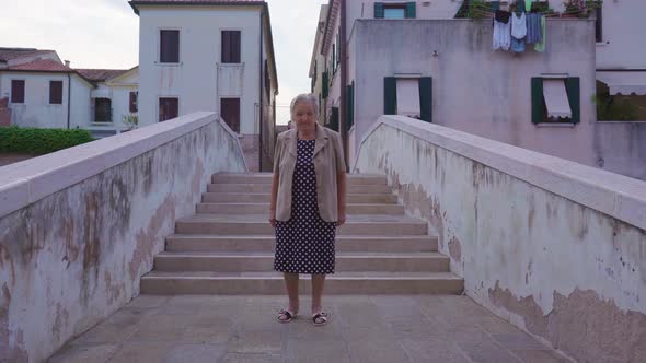 Senior Woman Traveler Stands on City Bridge in Chioggia