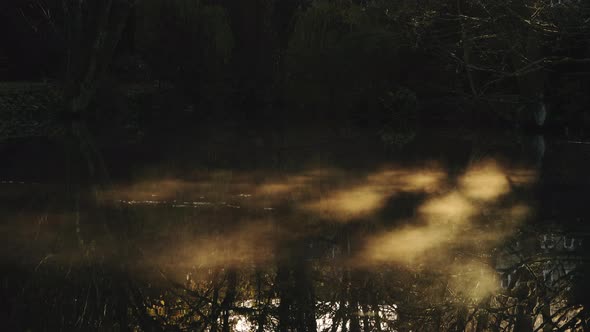 Mist moving on a lake in sunlight with beautiful orange reflections and sunshine shining on the mist