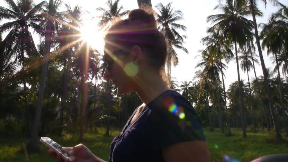 Female Using Smart Phone Against Sun Beams alt