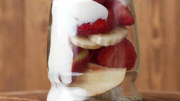 Fresh Fruit Yogurt with Bananas, Strawberries, Apples in a Jar Rotated on the Table