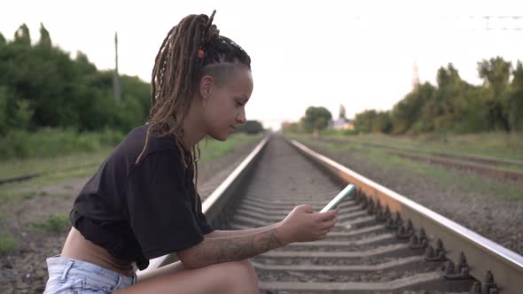 A Woman Uses a Smartphone on the Background of the Railway