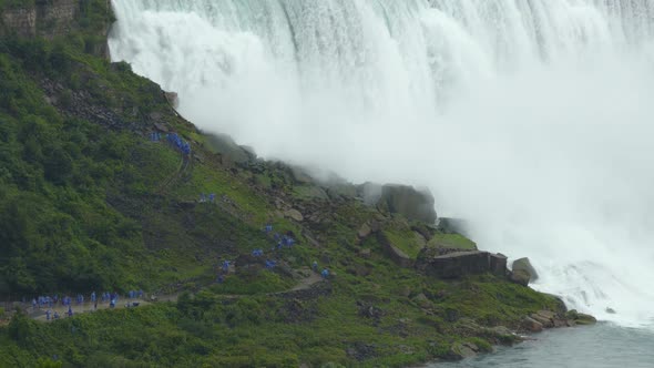 People hiking near Niagara Falls, next to powerful water flowing down the waterfall creating steam,