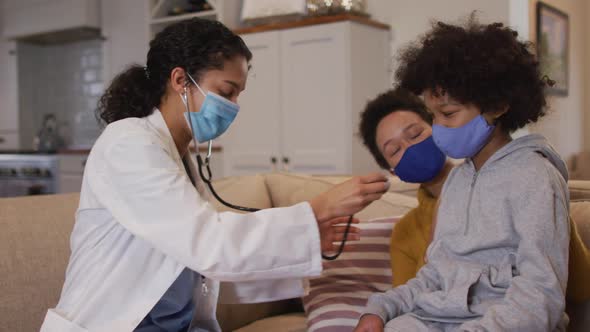 Mixed race female doctor wearing mask examining mixed race girl at home
