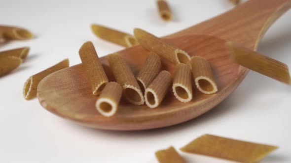 Falling dry uncooked integral pasta in slow motion into a wooden spoon