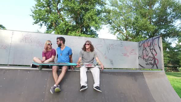 Cool young friends sitting on a ramp at skatepark and chilling