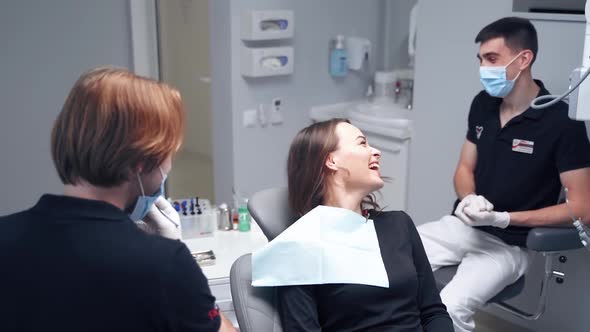 Smiling woman in stomatology clinic. Male dentist talking to a patient while showing jaw model. 