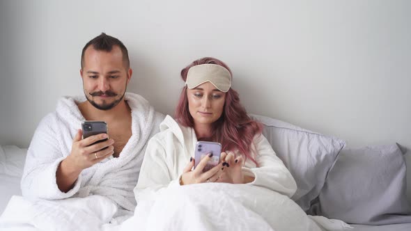 Caucasian Couple Using Smartphone Lying on Bed Together Checking Social Networks News in the Morning