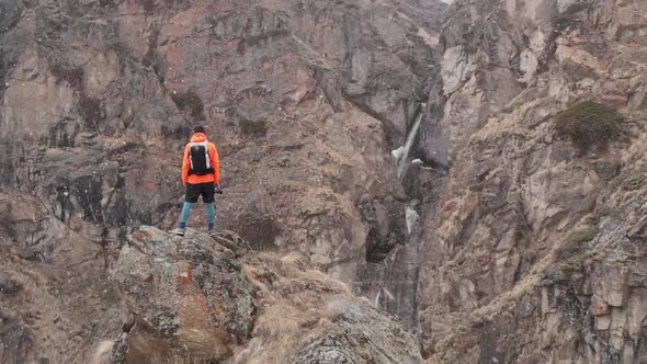 Aerial View of a Young Male Photographer with a Camera in His Hands Stands on a High Rock in a Gorge