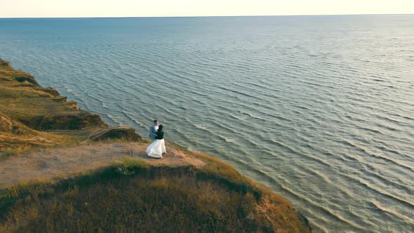 Aerial View A Couple of People Stand on the Edge of a Cliff and Watch the Beautiful Sunset at Sea