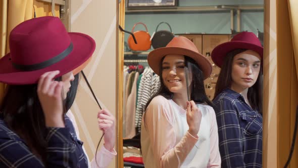 Two Young Lovely Women Trying on Hats, While Shopping Together