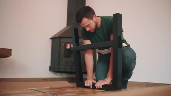 Young Man Assembling Leg Of DIY Table On The Floor. - wide shot