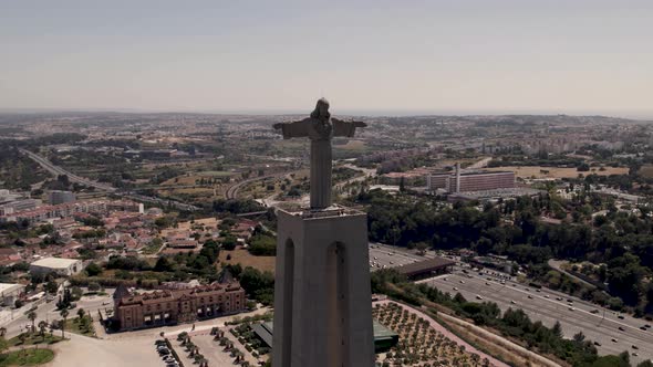 Front facing of majestic statue of Christ the King against Almada cityscape, aerial panning shot.