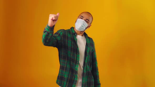 African American Guy in Medical Mask Showing Thumbs Up Gesture Against Yellow Background