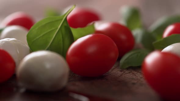 Camera follows pouring olive oil over cherry tomato and mozzarella cheese salad. Slow Motion.