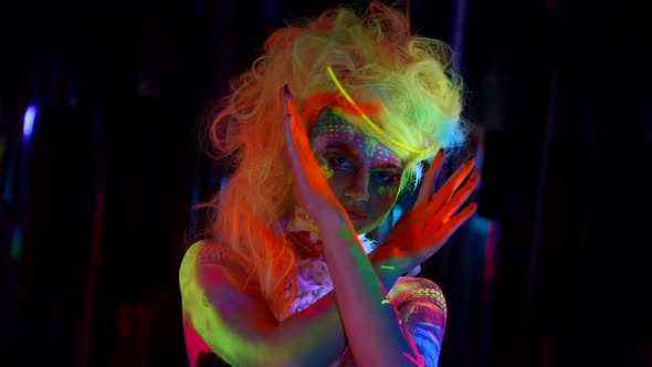 Actress of Circus with Bright Fluorescent Makeup and Suit Posing to Camera in Darkness
