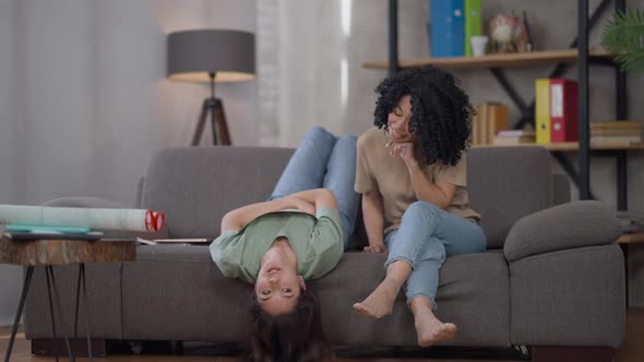 Wide Shot of Slim Charming Asian Woman Lying Upside Down on Couch Holding Business Graph Talking to