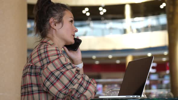 Caucasian Woman Talking By Phone During Working with Laptop in Coffee Shop