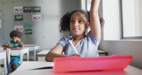 Video of happy biracial girl raising hand during lesson in classsroom