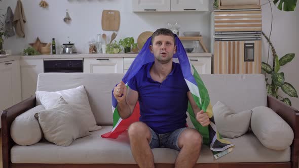 A White Male Sports Fan Watches TV at Home with the South African Flag