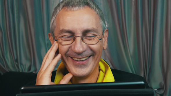 Laughing Man in Glasses Reading a Tablet